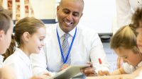 A teacher works with students seated around a table.