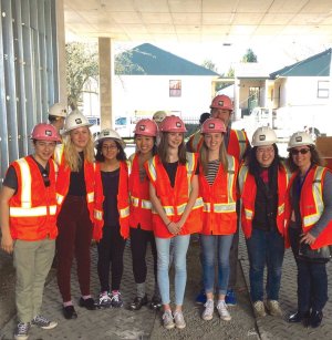 A group of high school students wearing orange vests and hard hats stand together.