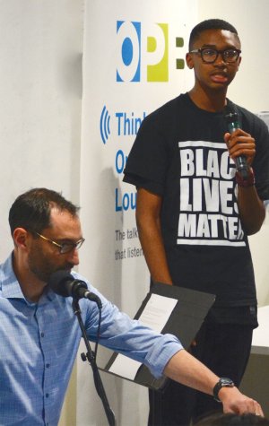 A high school student is speaking into a microphone in front of an audience.