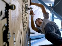 A low angle shot of a young teen boy leaning against a large wooden clock, more than twice his size, using a wrench.