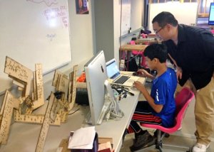 Boy in studio working at a computer with adult looking on