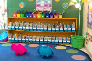 A bookshelf, circular rug, and two portable rocking chairs in the corner of a classroom.