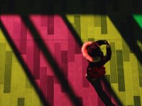 An aerial shot of a girl in a coat holding a cell phone up to her face. She's standing on a floor that's pink, yellow, and green from the lights shining down on it.