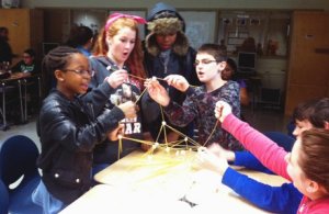 Students gathered around a desk connecting pasta into a modular structure