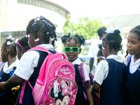 Group of students, many wearing backpacks, and one girl wearing neon green sunglasses