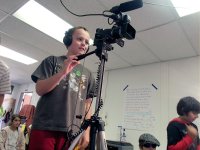 Boy wearing headphones standing in class operating a camera on a tripod