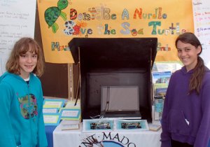 Two girls standing at a booth that has lots of reading material and turtle facts up on the walls