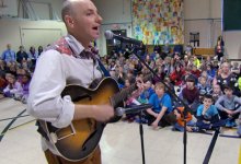 Man singing and playing the guitar in the gym full of students and teachers