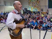 Man singing and playing the guitar in the gym full of students and teachers