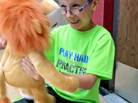 A young boy in a bright green shirt and glasses is smiling, holding a stuffed lion doll, looking straight into its face