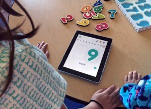 Two children at desk looking at numbers on a tablet