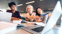 Three students discuss information they’re reading on a laptop.