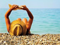 Woman in hat laying on beach reading with ocean view