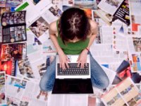 A photo of a female high school student working on a laptop, surrounding by articles.