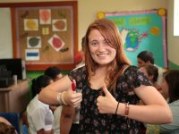 Girl in a classroom standing in front of students working giving two thumbs up