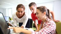 Three students discuss work on a computer and a tablet as they build an app.