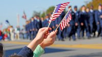Picture of two people waving small U.S. flags with a memorial day parade in the background