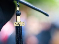 A black graduation tassel with 2016 in gold lettering is hanging from a black graduation cap. 