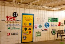 An outdoor covered hallway with 25+ logos painted on the wall and door
