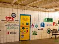 An outdoor covered hallway with 25+ logos painted on the wall and door