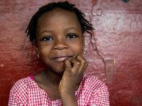 A closeup of a young girl, close-mouth smiling, with her chin resting on her right hand. 