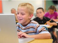 Boy at his desk laughing at something on his laptop
