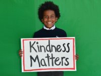 photo of a student holding a sign which reads "Kindness Matters"