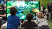 Facing a large monitor, three elementary school-aged boys play a video game. 