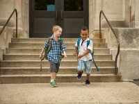 Two young boys wearing backpacks rushing down the front steps of school 