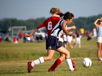 Two teen girls are fighting for a ball on the soccer field.