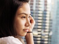 A closeup of a side profile of a young female student looking out a window. Her left cheek is resting against her left hand, and there's a hair tie around her wrist.