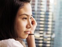 A closeup of a side profile of a young female student looking out a window. Her left cheek is resting against her left hand, and there's a hair tie around her wrist. 