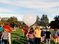 A classroom of kids and teacher out on the field getting ready to release a weather balloon