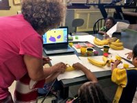 Woman doing a project with young kids using bananas and Play-Doh with a laptop in the center of the table open to an app