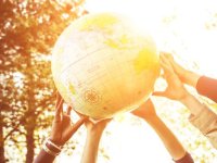 Many hands lifting up a large beach ball that looks like a globe