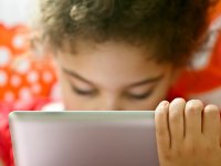 A laptop screen in the foreground with a blurred student behind the screen.