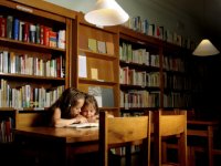 Two young girls huddled together reading a book in the library