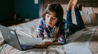 Teenage girl working on school work with her laptop on her bed