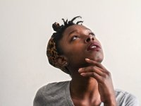 A closeup of a young teenage girl looking up with her head tilt back and her hand under her chin.