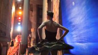 A female ballet dancer standing on the side of a stage about to dance.