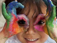 Little girl looking through hands covered in paint like glasses