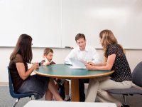 Mom, dad, and boy speaking with teacher around a table