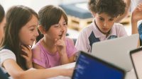 Elementary students work together on a laptop