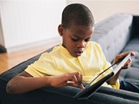 Boy sitting at end of a couch working on a tablet