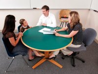 Young boy sitting between and woman and man at a round table with a teacher sitting across from them holding papers