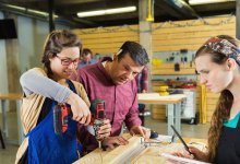 One student uses a drill under supervision while another takes notes.