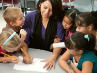 Teacher writing with a pencil surrounded by five young engaged students