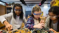 Three girls work on computer circuitry.