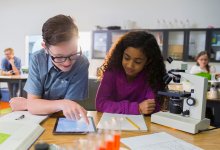 A young boy and girl work together with a microscope and an iPad.
