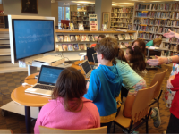 Photo of a group of students sitting around a computer lab table in the school library.
